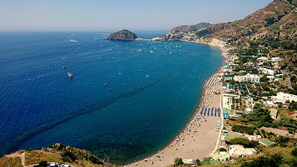 Stunning coastal view with boats in clear blue water and vibrant shoreline, perfect for a sailing adventure.