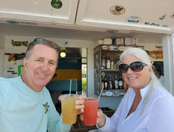 Mark and Sharon Noneman enjoying tropical drinks at a sunny beach bar with a nautical theme
