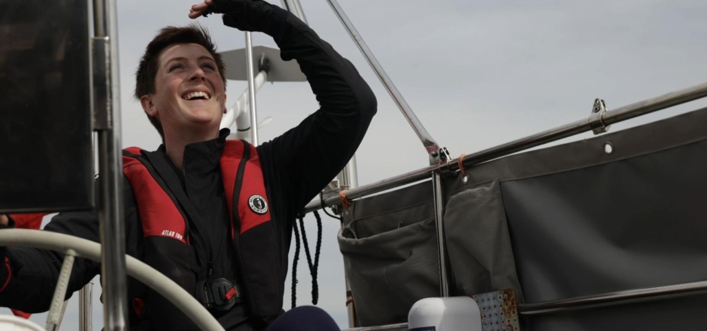 Smiling sailor navigating on yacht with confidence, wearing red life jacket, enjoying adventurous sailing trip.