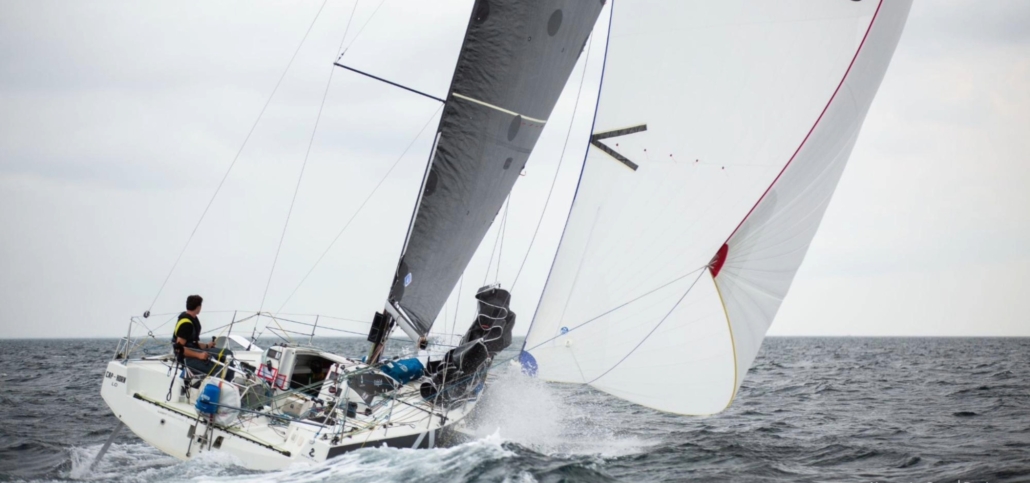Sailboat navigating choppy seas, crew member steering, sails full in the wind.