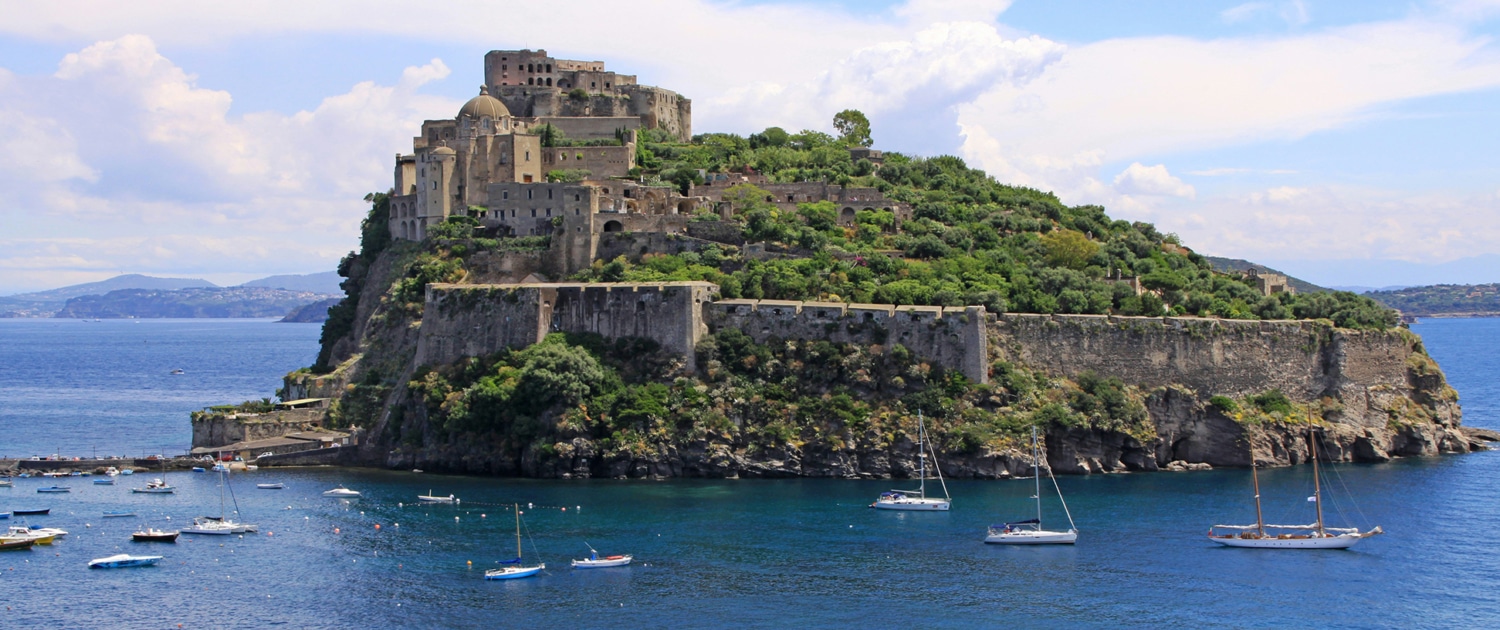 Sailing boats near a historic island fortress surrounded by the blue sea, highlighting scenic and adventurous travel.