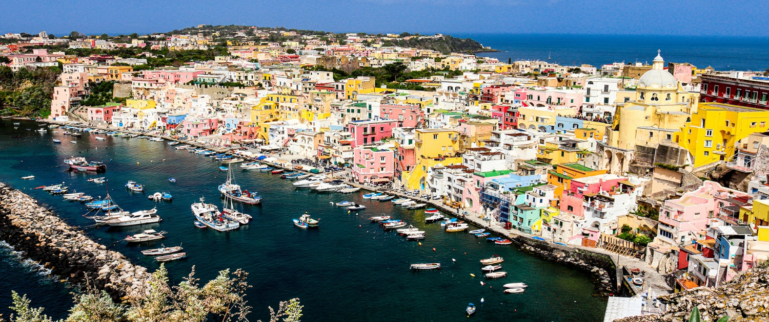 Colorful port town with boats docked in vibrant harbor, scenic view with blue sky and sea background.