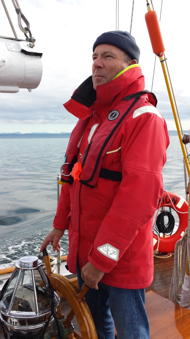 20161028_113703 Man in red jacket steering sailboat on calm water.