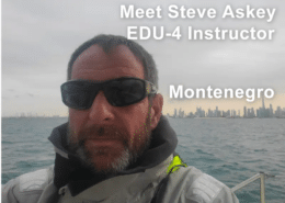 Steve Asley sailing in Montenegro, wearing sunglasses and sailing gear, city skyline in the background.