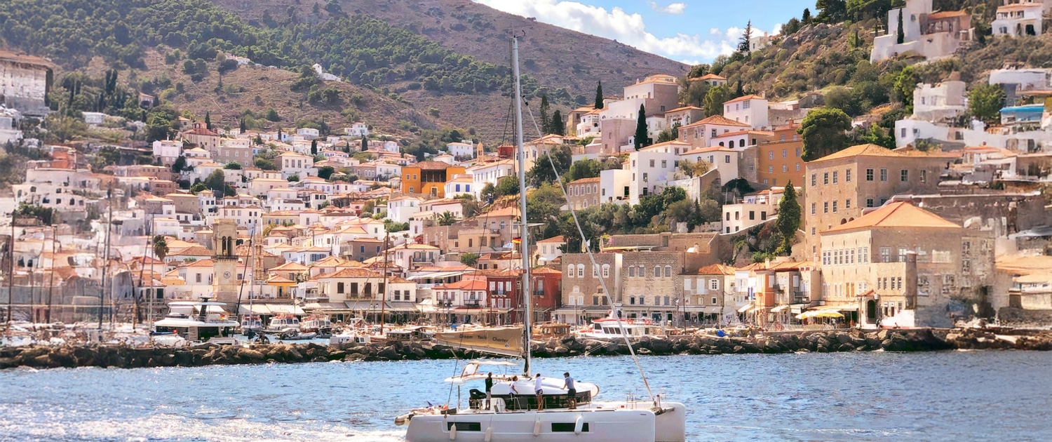 Sailing yacht in vibrant Greek harbor with hillside views, clear skies, and charming architecture. Perfect summer getaway.