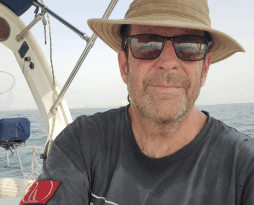 sa boat .jpeg Man enjoying a sunny day sailing on the open sea, wearing a hat and sunglasses for sun protection.
