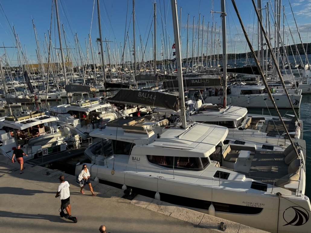TROGIR Catamarans docked at a marina with clear blue skies, people walking along the pier.