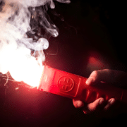 blog-featured-image-4-emergency-flares-101 Hand holding a lit distress flare with sparks and smoke, essential for boating safety and emergency signaling.