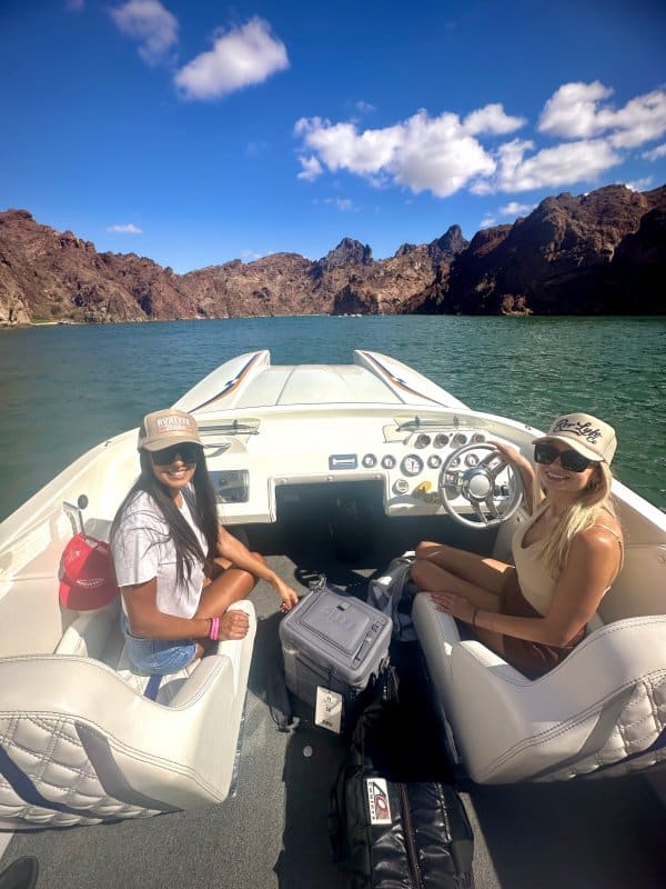instructor_969_2065 Two women enjoying a sunny boat ride in a scenic rocky canyon with clear skies and calm water.
