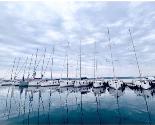 George Sakkas Docked sailboats lined up under cloudy skies, reflecting on calm water.