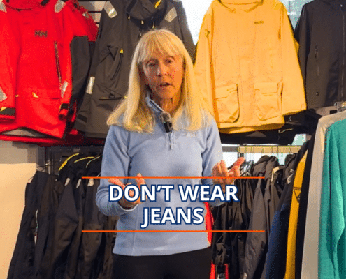 Woman giving sailing attire advice, standing in front of waterproof jackets, with text overlay: Don't Wear Jeans.