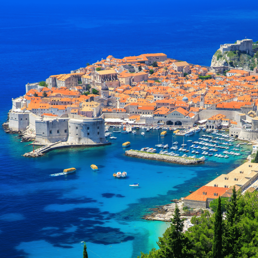 blog-below-deck-destinations-11-Dubrovnik Scenic view of a vibrant Adriatic coastal city with red-roofed buildings, a bustling harbor, and clear blue waters.