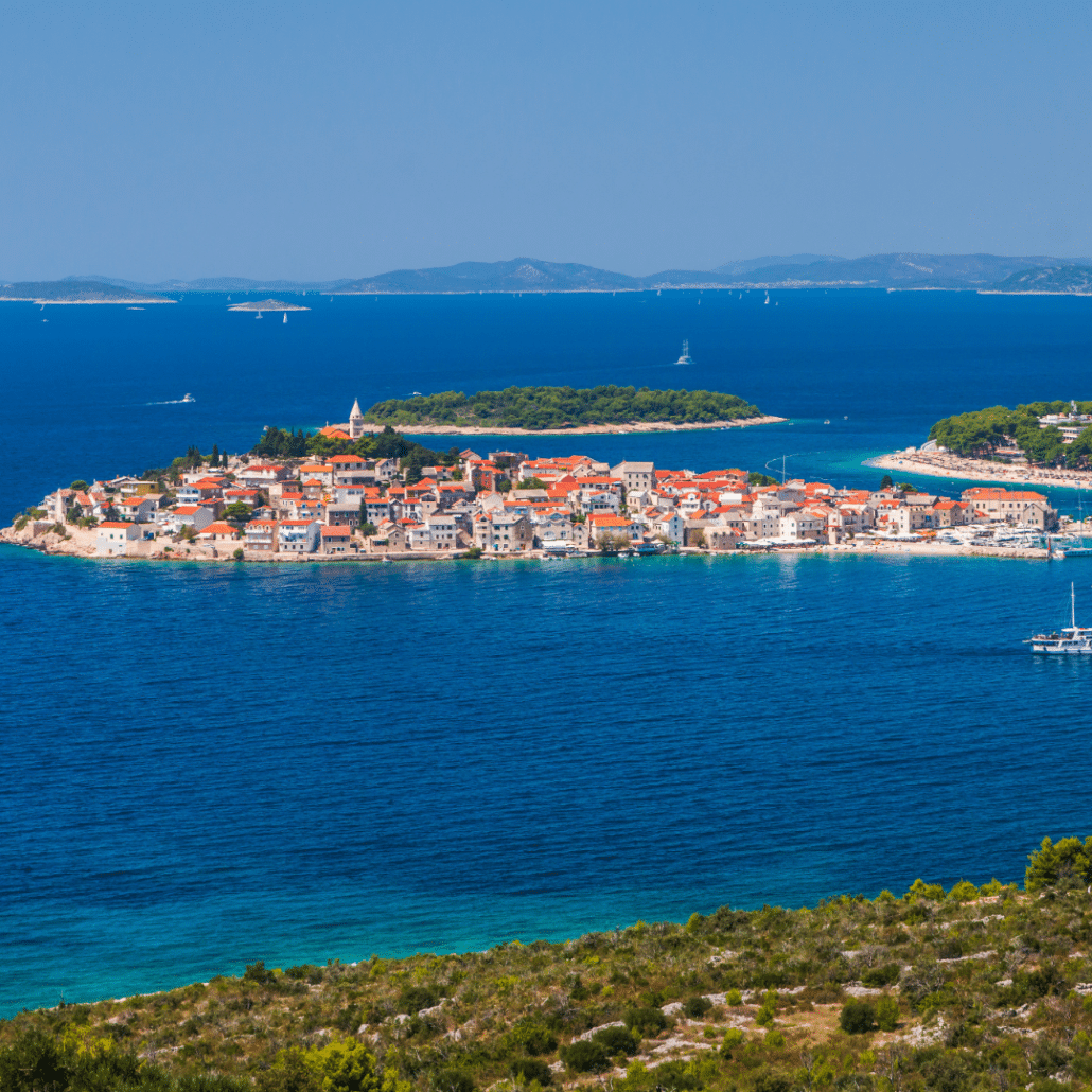blog-below-deck-destinations-6-Šibenik Scenic island village with red rooftops, surrounded by emerald sea, perfect for sailing adventures and coastal exploration.