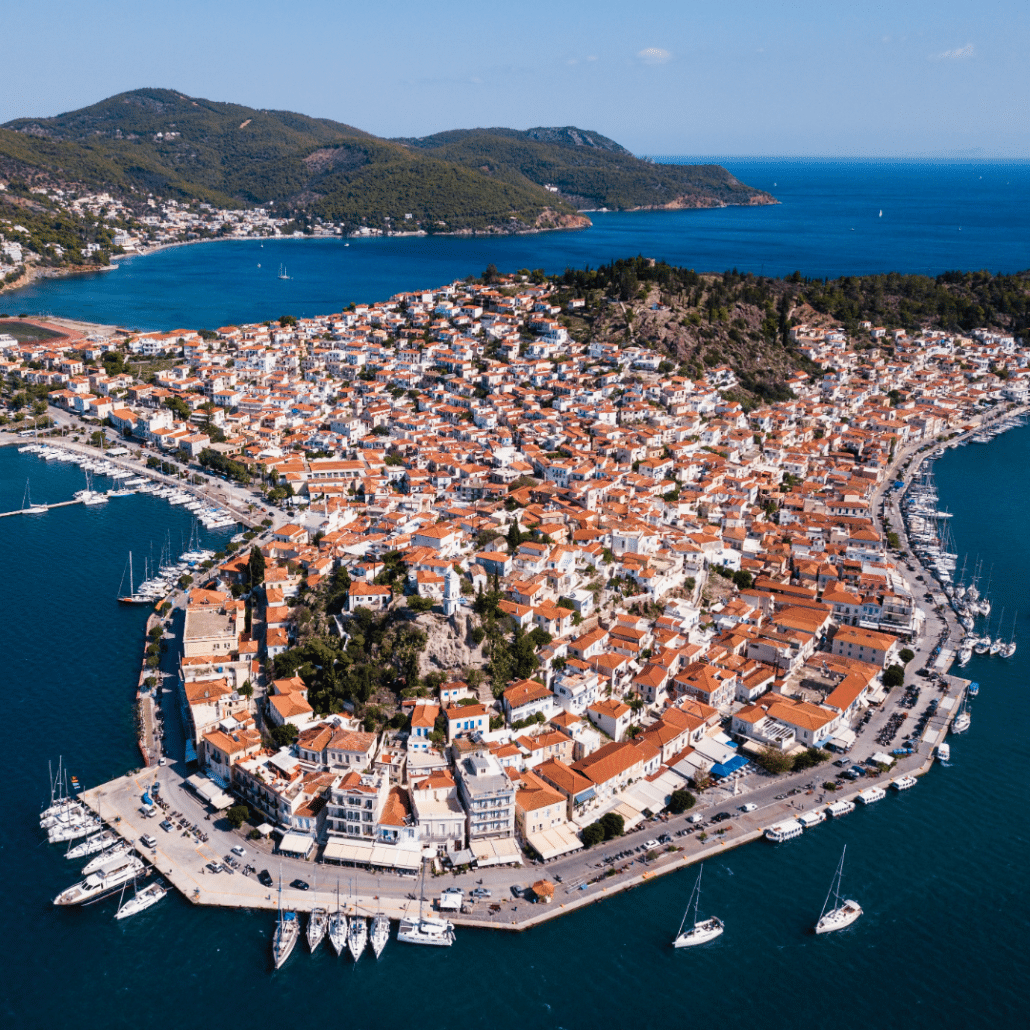 blog-below-deck-destinations-9-Saronic Gulf Aerial view of a vibrant coastal town with marina, sailboats, and rolling hills, perfect for a sailing adventure.