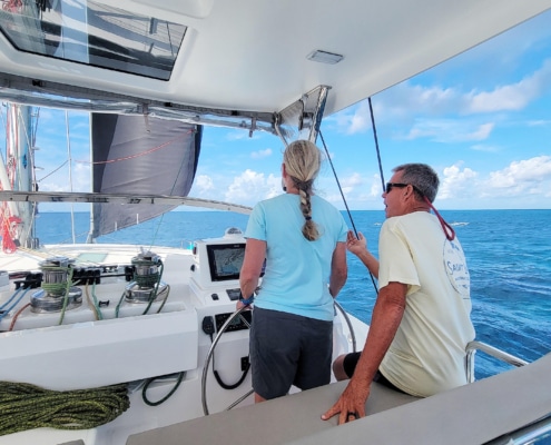 Bill Ibsen Sailors navigating a catamaran on open blue waters under a clear sky, with another sailboat visible in the distance.