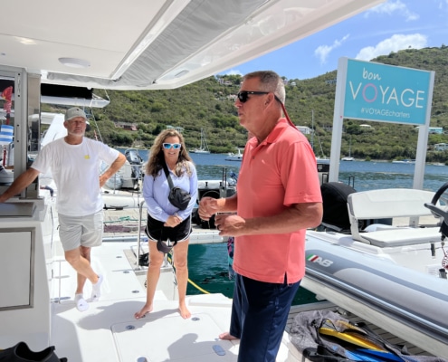 Bill Ibsen People aboard a yacht, ready for a sailing adventure. Sign reads Bon VOYAGE with scenic harbor view.