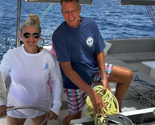 Bill Ibsen Two people enjoying a sunny day sailing, managing ropes, and steering on a boat with a blue ocean backdrop.