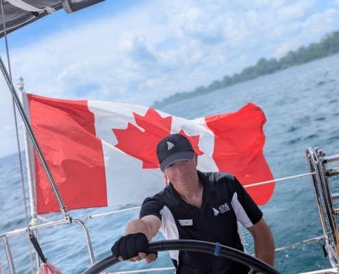 Robert Frigault Sailor navigates a yacht with a Canadian flag, symbolizing adventure and patriotism on open waters.
