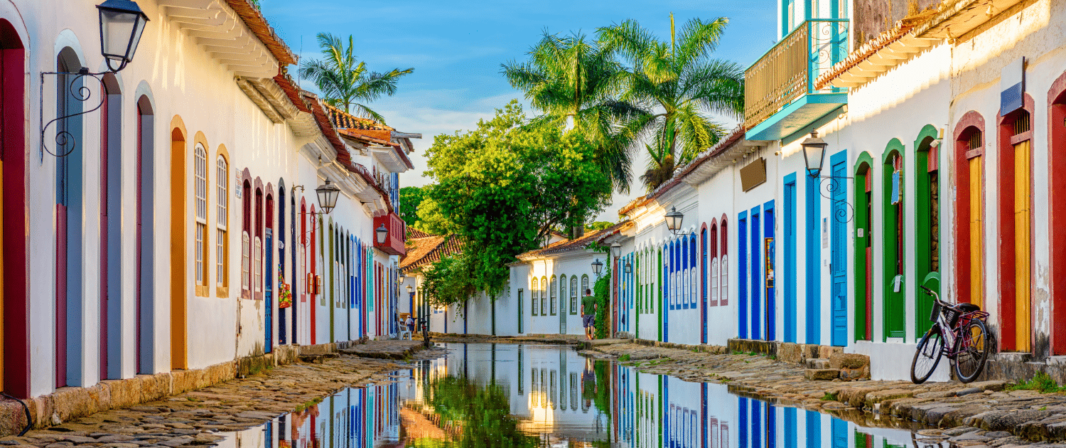 Colorful colonial street mirrored in water, with vibrant doorways, a bicycle, and lush greenery under clear blue skies.