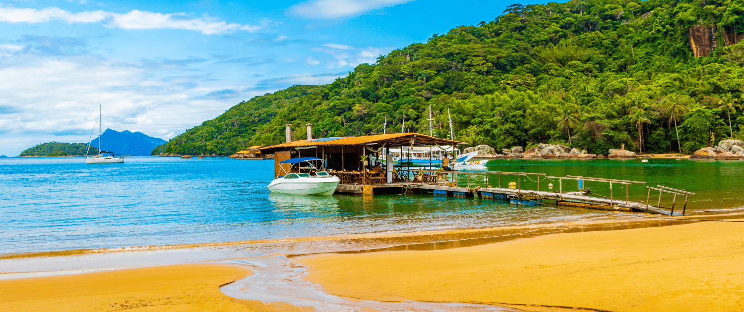 Tropical beach bar with a dock, boats, and lush green hills in the background, perfect for a sailing getaway.