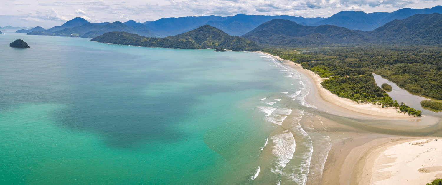 Panoramic view of a coastal landscape with turquoise waters, sandy beaches, and lush green mountains under a cloudy sky.