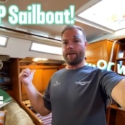 Man inside sailboat cabin with CHEAP Sailboat! and SALE text overlay. Bargain sailboat exploration.