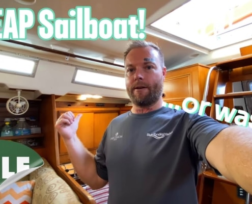 Man inside sailboat cabin with CHEAP Sailboat! and SALE text overlay. Bargain sailboat exploration.