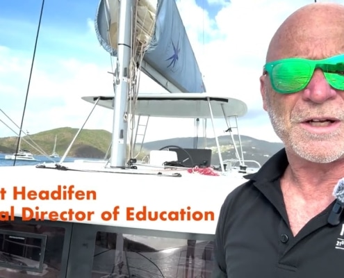 A person on a sailboat with lush islands and boats in the background, wearing green sunglasses and a NauticEd shirt.