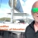 A person on a sailboat with lush islands and boats in the background, wearing green sunglasses and a NauticEd shirt.