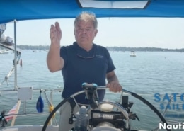 Man steering sailboat with confidence on a sunny day, showcasing sailing gear and open water scenery.