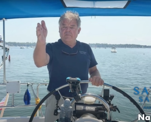 Man steering sailboat with confidence on a sunny day, showcasing sailing gear and open water scenery.